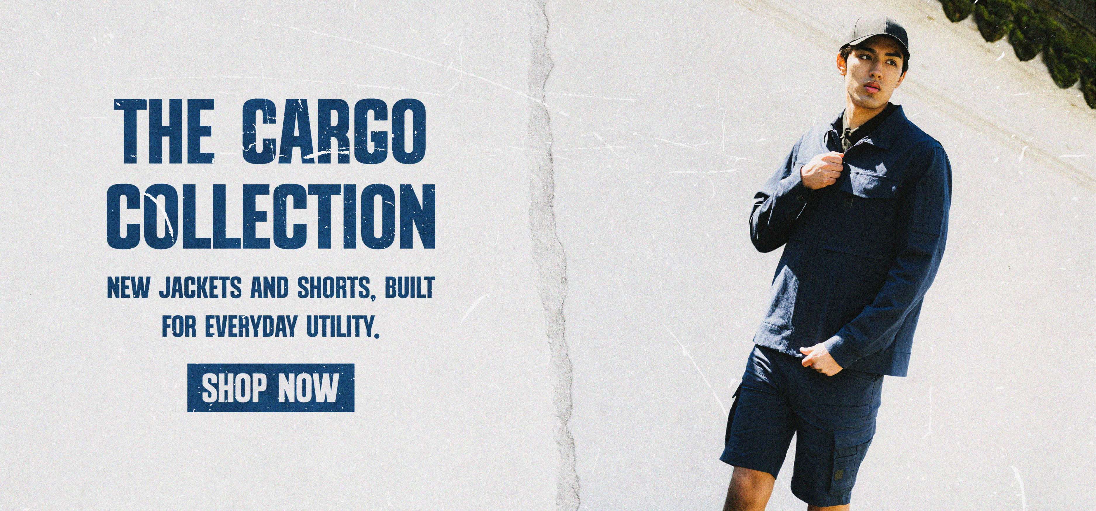 Promotional banner for the Cargo Collection featuring a model wearing a navy cargo jacket and matching cargo shorts outdoors. Large headline reads “The Cargo Collection” with supporting text “New jackets and shorts, built for everyday utility” and a “Shop Now” call-to-action button.